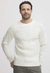 Hvit kabelstrikket genser med teksturerte mønstre og ribbede mansjetter, med klassisk rund hals og avslappet passform.