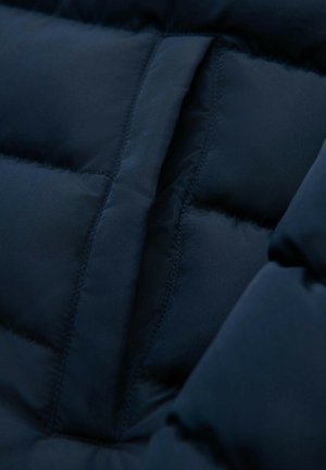 Navyblauwe pufferjack detail, met gevulde panelen met een gladde textuur en subtiele naden, die de warmte en het gewatteerde ontwerp benadrukken.