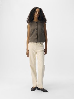 Top sans manches marron avec des boutons devant, associé à un pantalon droit beige clair et des chaussures à bout pointu marron foncé. Texture de tissu lisse.