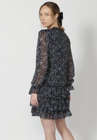 Rochie neagră cu flori, cu mâneci lungi transparente, tiv ondulat și motive florale albastre și albe. Are un decolteu rotund și o croială lejeră.