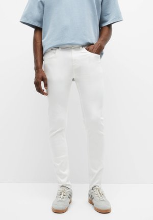 Jeans en denim blancs avec une coupe slim, dotés de cinq poches et de coutures contrastantes. Associés à un t-shirt surdimensionné bleu clair et des baskets grises.