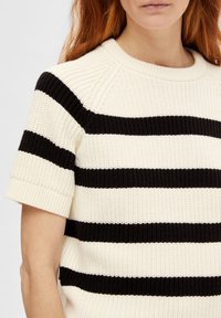 Strikket kortærmet sweater med skiftende sorte og creme horisontale striber. Ribbet rund halsudskæring og opkrøllede ærmer.
