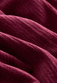 Tessuto bordeaux con una superficie morbida e strutturata, caratterizzato da onde delicate e un motivo a coste, che trasmette profondità e interesse visivo.