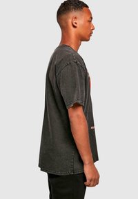 Gray cotton oversized T-shirt with short sleeves, crew neck, and distressed hem. Features multicolored graphic on the front with text.