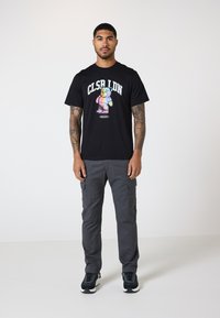 Sort t-shirt med et farverigt bjørne-tryk og teksten "CLSR LDN". Sæt sammen med grå cargo-bukser med lommer og sorte sneakers.