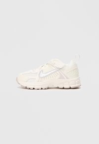 Sapatilhas de tom bege claro com parte superior em rede, detalhes texturizados e o swoosh da Nike em branco. Possui bico arredondado e sola almofadada para conforto.