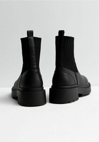 Stivali neri alla caviglia con una finitura in pelle testurizzata, pannelli laterali elastici e suole nere spesse. Caratterizzati da un anello sul retro per facilitarne l'indossamento.