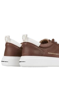 Sneaker in pelle marrone con dettagli bianchi, caratterizzati da una finitura testurizzata, punta rotonda, tacco piatto e dettaglio del logo dorato sul retro.