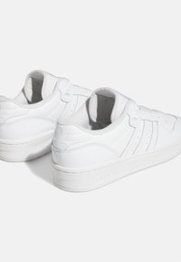 Vita atletiska sneakers med slät läderöverdel, tre horisontella ränder, vadderad krage och texturerad gummisula.