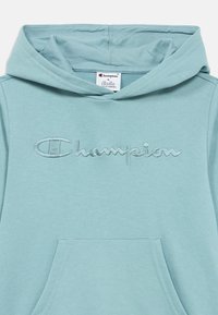 Φωτεινό γαλάζιο φούτερ με κουκούλα και τσέπη καγκουρό, με κεντημένο λογότυπο "Champion" σε αντίστοιχο χρώμα στο στήθος, φτιαγμένο από μαλακό υλικό.