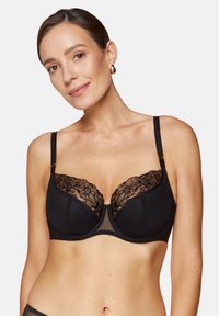 Czarny biustonosz z przejrzystymi miseczkami, koronkowymi detalami, regulowanymi ramiączkami i gładkim pasem pod biustem. Kwiatowy wzór na koronce dodaje tekstury i detali.