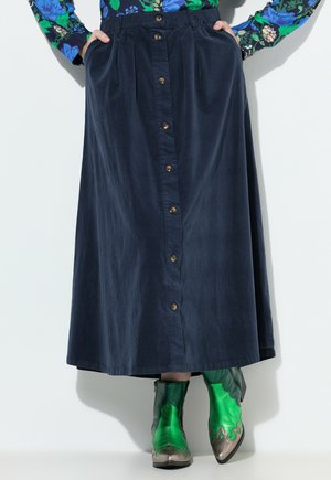 Marineblauwe, knielange rok van katoen met plooien en voor knopen. Gecombineerd met groene metallic enkellaarzen met decoratieve accenten.