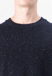 Granatowy sweter robiony na drutach z okrągłym dekoltem, z teksturowanym wzorem i drobnymi plamkami jaśniejszych kolorów w całym materiale.