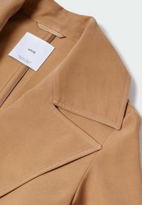 Light brown tailored jacket with sharp lapels, smooth texture, and inside label visible. Features clean lines and structured design elements.