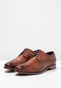 Chaussures habillées en cuir marron avec un détail perforé et un bout arrondi, dotées d'un laçage et d'un petit talon empilé.