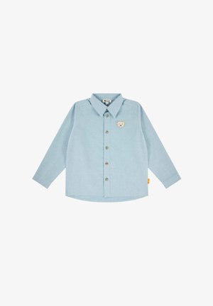 Lange mouwen shirt van lichtblauwe stof met een knoopsluiting aan de voorkant, een puntige kraag en een berenpatch op de borst. Ronde onderkant.