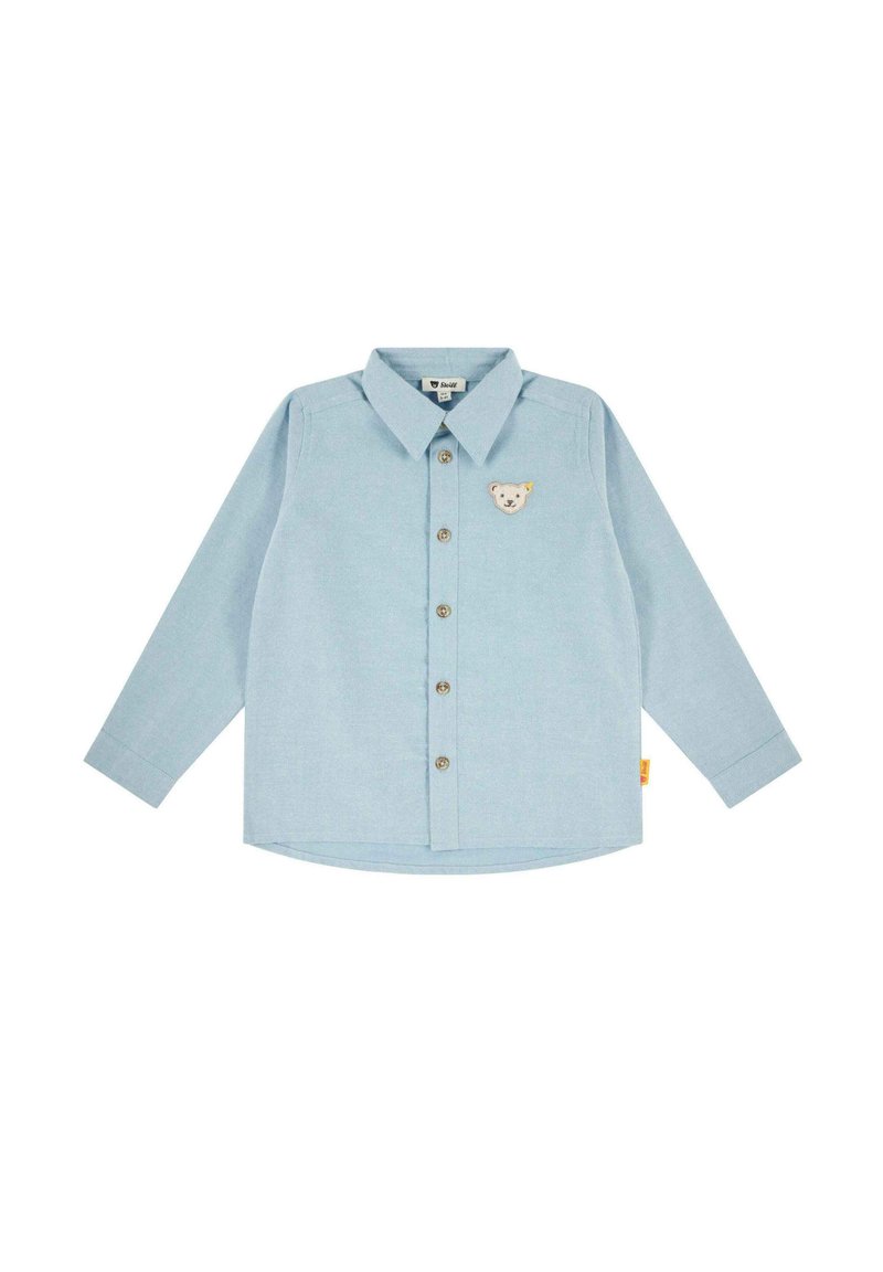 Camicia a maniche lunghe in tessuto azzurro chiaro con chiusura a bottoni, colletto a punta e una patch a forma di orso sul petto. Orlo arrotondato.