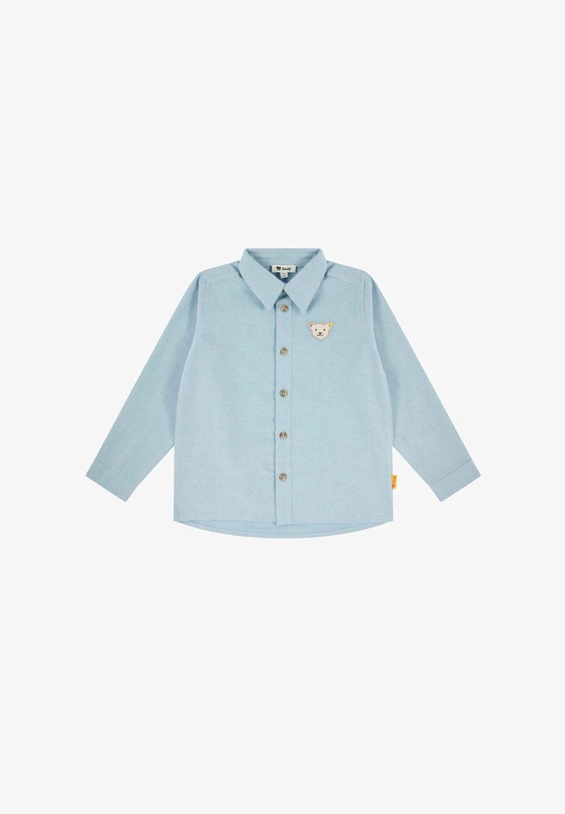 Halenka s dlouhým rukávem v světle modré barvě, s knoflíkovým zapínáním vpředu, špičatým límcem a nášivkou medvěda na hrudi. Zaoblený lem.