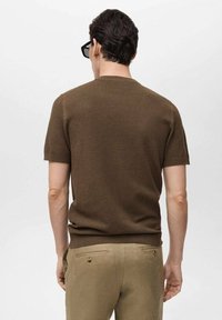 Maglione corto a maniche corte marrone, con scollatura rotonda, forma aderente e orlo a coste, abbinato a pantaloni kaki chiari.