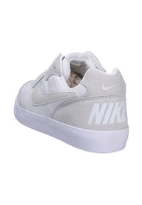 Zapatilla blanca con un upper de tela texturizada, acentos en ante gris, un collar acolchado y un gran logo blanco de "NIKE" en el talón.