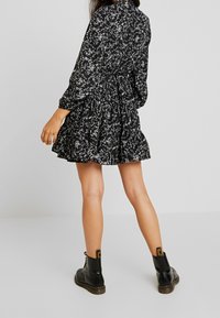 Svart blommig klänning med långa ärmar, midjeband och volang i nederkant, bärs med svarta ankelboots; mjukt tyg med vitt blommönster.