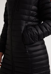 Cappotto imbottito nero con design a righe orizzontali, colletto alto, zip frontale e tasche laterali. Texture liscia con isolamento leggero.