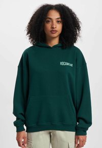 Green hooded sweatshirt with a relaxed fit, featuring a front pocket and "ROCAWEAR" logo in white on the left chest area. Cotton material.