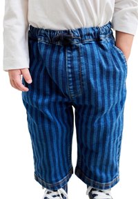 Pantaloni din denim cu dungi albastre, talie elastică, buzunare laterale și tivuri răsucite. La bază se văd o pereche de adidași albi.