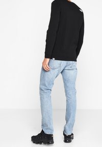 Černá dlouhá rukávová košile s logem, světlé modré džínové kalhoty a černé tenisky. Tento outfit má volný střih a jednoduchý design.