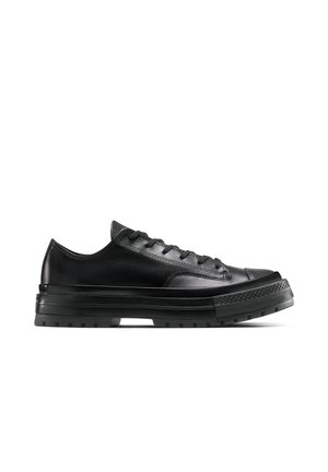 Niedriger schwarzer Ledersneaker mit dicker Gummisohle, strukturierter Zehenkappe und schwarzen Schnürsenkeln, seitlich auf weißem Hintergrund gezeigt.