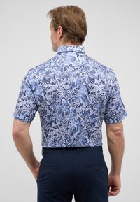 Korte mouw overhemd in lichtblauw met een bloemmotief in donkerblauw en zwart. Heeft een klassieke kraag en een reguliere pasvorm.