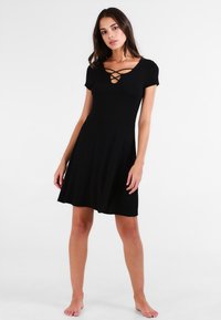 Czarna sukienka z dopasowanym topem i rozkloszowanym dołem, z krótkimi rękawami i krzyżującym się detalem przy dekolcie. Gładka tekstura.