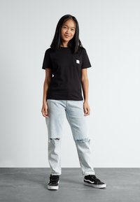 Svart bomull t-skjorte med korte ermer og lomme på venstre bryst, sammen med lyseblå ripped jeans og svarte joggesko.