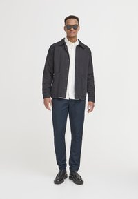 Temno jakno z gumbno zapiranjem, belo srajco in mornarsko modre hlače. Črna sončna očala in loaferji za popoln izgled. Gladek material, sodoben kroj.