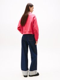 Felpa corta rosa con scollatura tonda, abbinata a jeans a gamba larga blu scuro con polsini grigi strappati e scarpe nere basse.