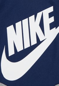 Tamsiai mėlynas medvilnės audinys, ant kurio užrašytas didelis baltas "NIKE" logotipas su swoosh dizainu. Lygus paviršius su ryškiu, kontrastingu spalvų deriniu.