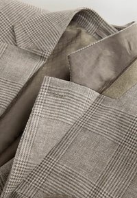 Detail béžovo-hnedého károvaného saka s hladkou vnútornou podšívkou s vzorom a klopovým golierom s výrezom.