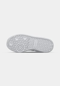 White sneaker sole with a textured tread pattern, featuring circular and triangular grips, and an embossed logo towards the heel.