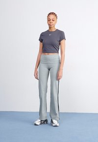 Grijze crop top en grijze sportbroek met zwarte zijstrepen, gecombineerd met zilveren sneakers, op een effen achtergrond.