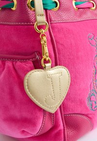 Borsa in suede rosa con accenti in pelle, presenta accessori in oro, un'etichetta decorativa a forma di cuore con la scritta "J" in rilievo e un cordoncino colorato.
