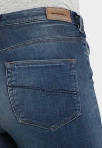 Jeans de mezclilla azul oscuro con una cintura de altura media, costuras visibles en los bolsillos traseros y una etiqueta de cuero con la marca en la parte posterior.