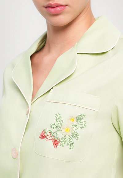 Light green pajama shirt with a soft texture; features a pocket with colorful strawberry and flower embroidery, and white piping along the edges.