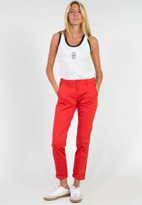 Un pantalon en coton rouge avec des ourlets roulés, associé à un débardeur blanc avec un contour noir. Les chaussures sont des baskets blanches avec une semelle beige.