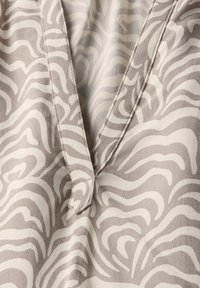 Beige stof med diskrete, bølgede, hvide zebra-lignende mønstre; har en V-halsudskæring og synlig syning detaljer.