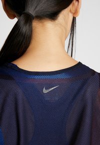 Maglietta atletica Nike con un design in rete testurizzata di colore blu scuro e dettagli in blu chiaro, che presenta un logo argentato all'altezza del collo sul retro.