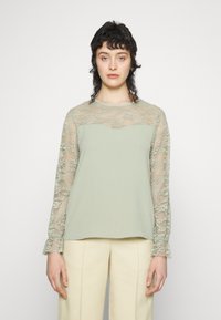 Top verde claro com mangas longas em renda. Textura canelada no corpo principal, padrão floral em renda nas mangas, decote redondo e punhos lânguidos.