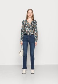 Blusa de flores de mangas longas em preto, azul e laranja com decote em V; combinada com jeans escuros ajustados e botas de tornozelo de cor clara.