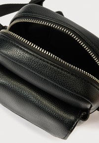 Mustast nahast ristisõlakott hõbedaste tõmblukkudega, millel on tekstureeritud pind, kaks taskut ja reguleeritav rihm.