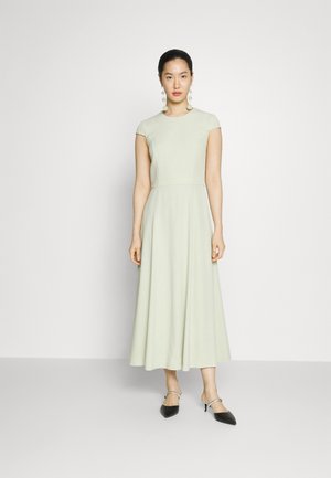 Lichtgroene jurk met kapmouwen, een getailleerde top en een uitlopende rok. Gladde stof, knielang, gecombineerd met zwarte slingback hakken.