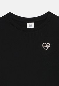 Black ribbed long-sleeve shirt with a round neckline and a small heart-shaped pink embroidered logo reading "GAP" on the left chest.
